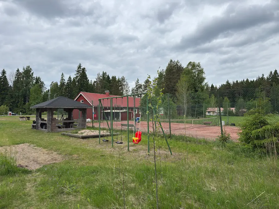 Pihapiiri — grillikatos, keinut, hiekkalaatikko ja tenniskenttä taustalla