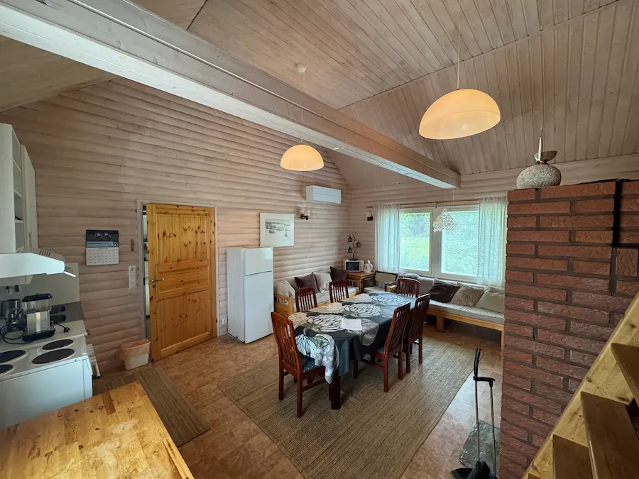 Takkatuvan ruokailutila toisesta kulmasta — pöytä, jääkaappi ja oleskelusohvat